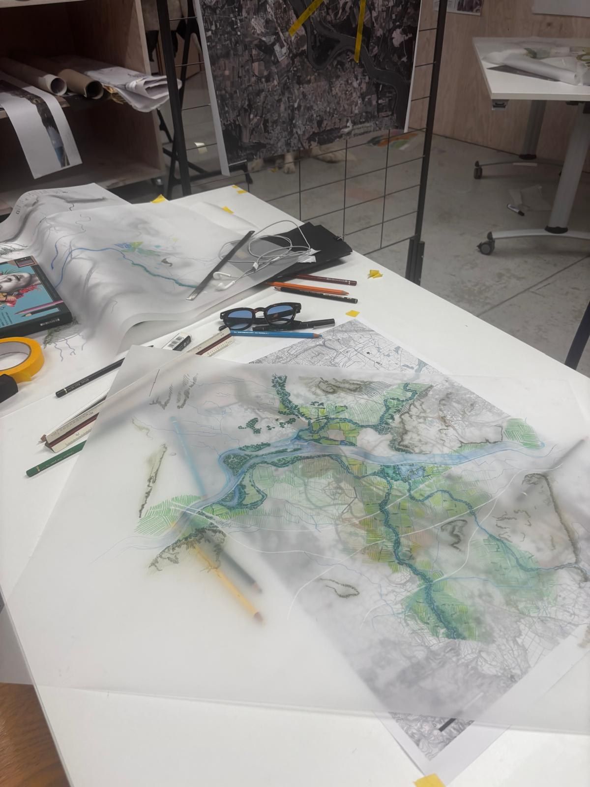 Calques de plan superposés sur une table d'atelier, crayons et ciseaux autour
