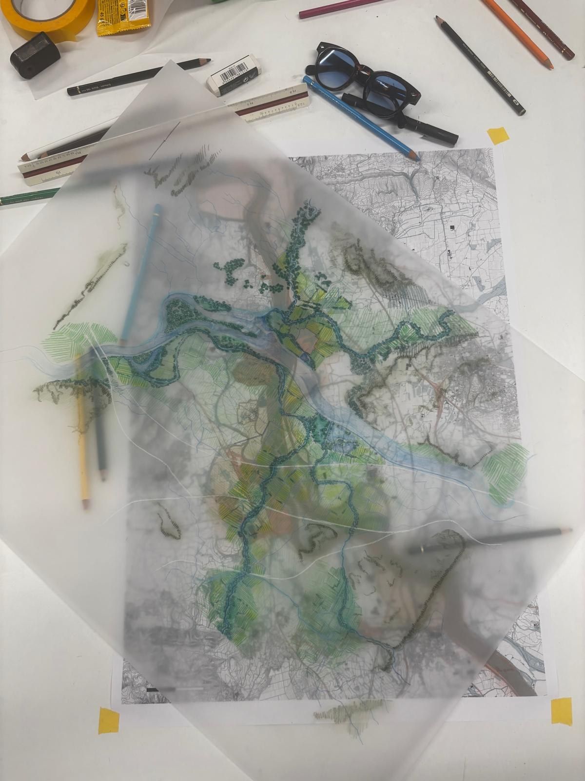 Calque de plan de paysage posé sur une table d'atelier, crayons de couleur autour