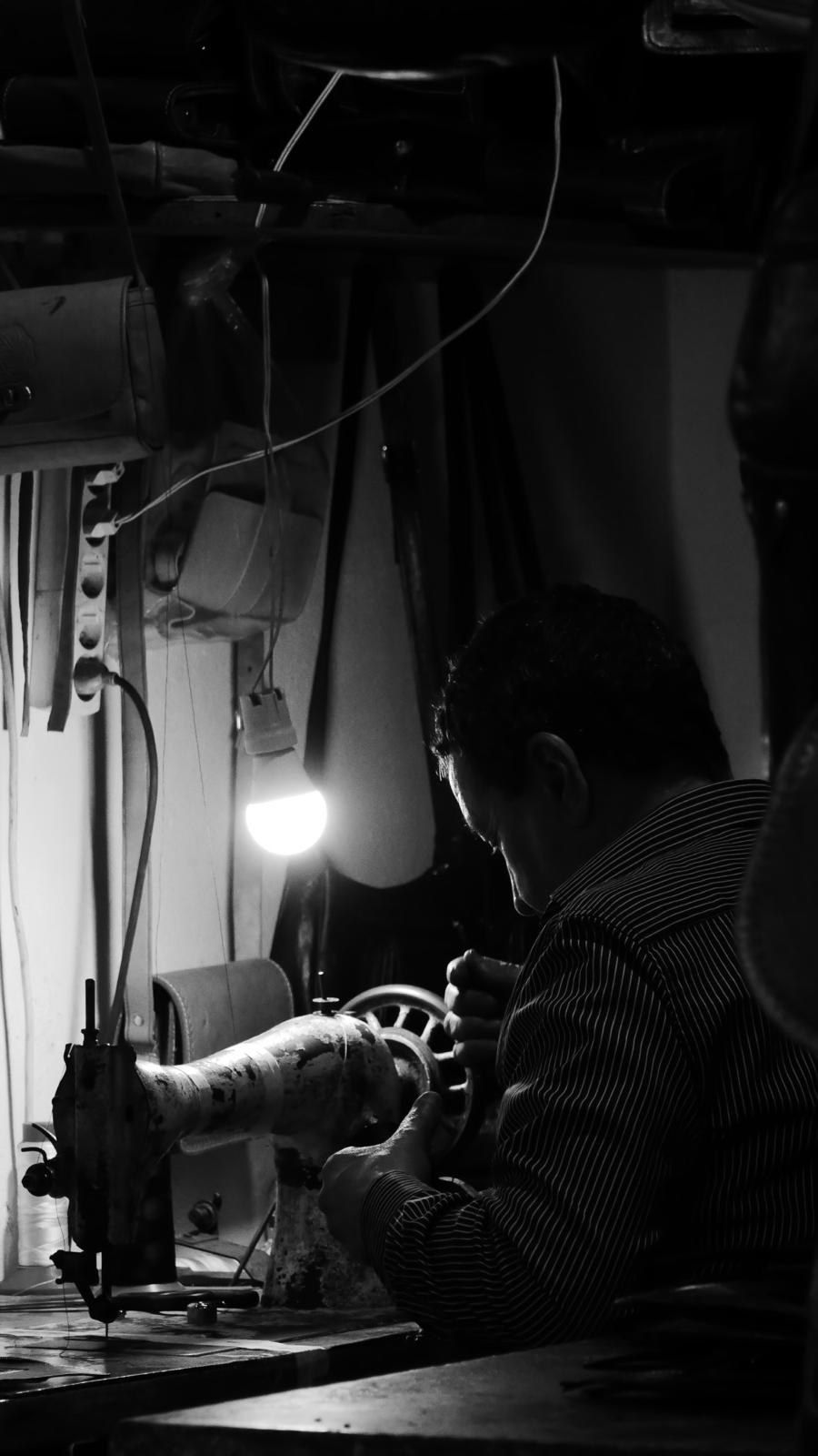 Atelier de couture éclairé par une lampe unique, un homme penché sur sa machine