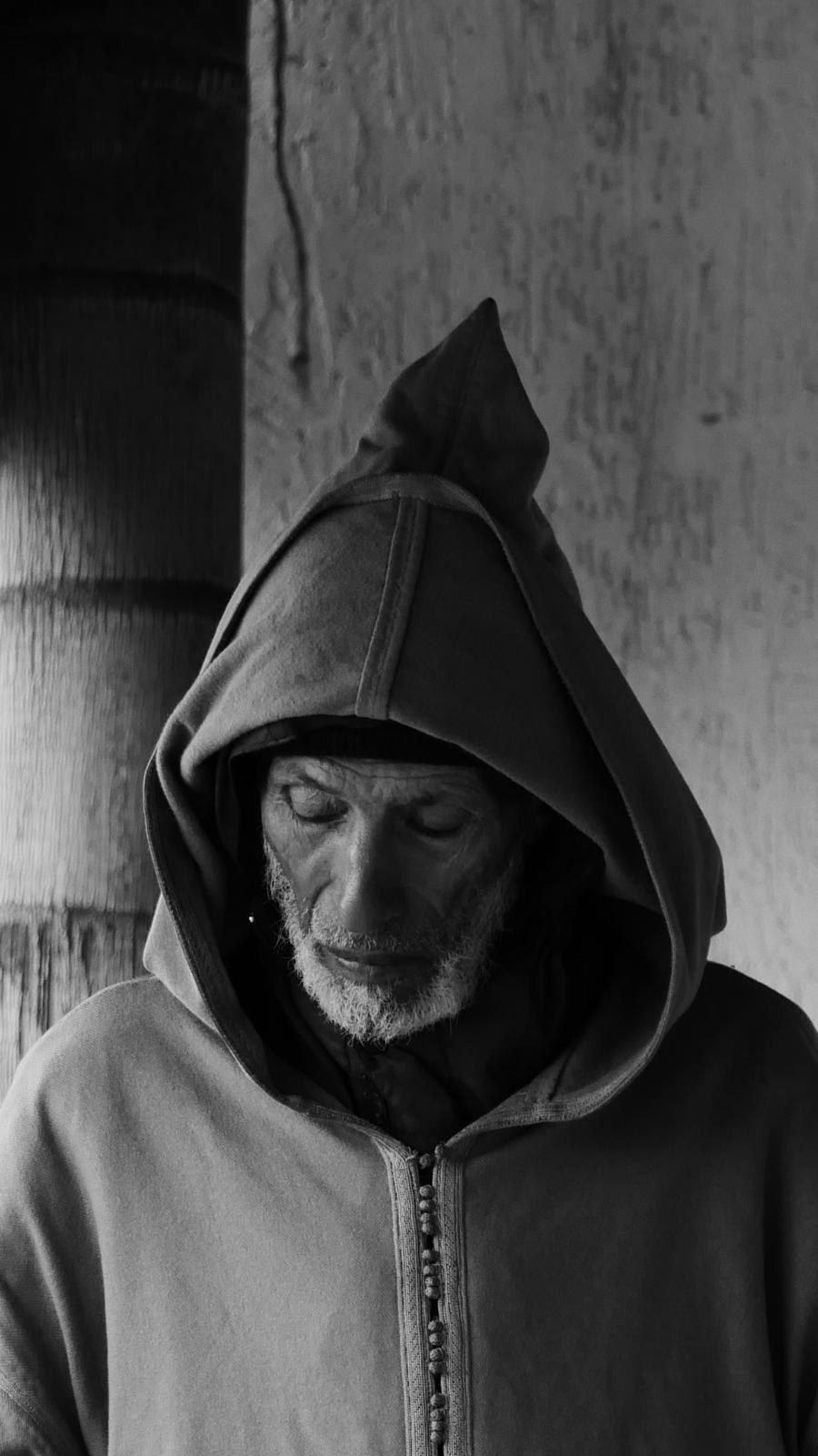 Portrait d'un homme âgé en djellaba à capuche, le regard baissé