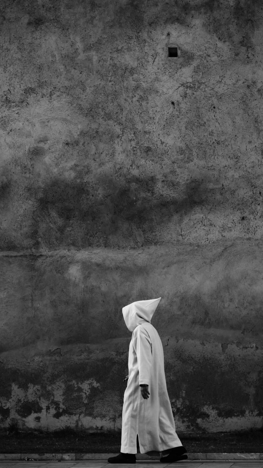 Silhouette en djellaba blanche traversant une grande façade nue